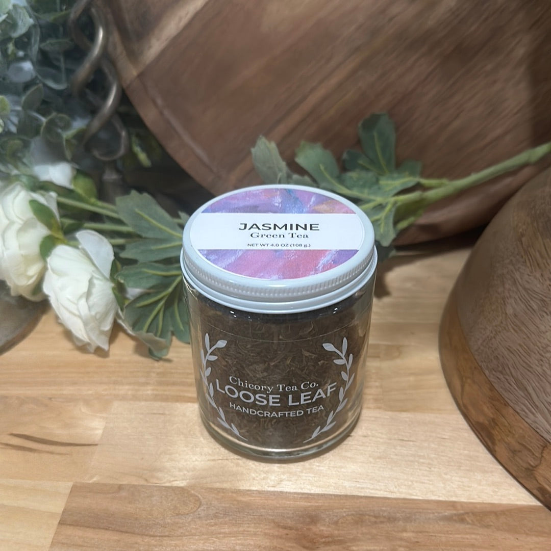 An artistic product photo of Chicory Tea Co.'s Jasmine Green Tea in the jar, from the front with flowers and a barrel in the background