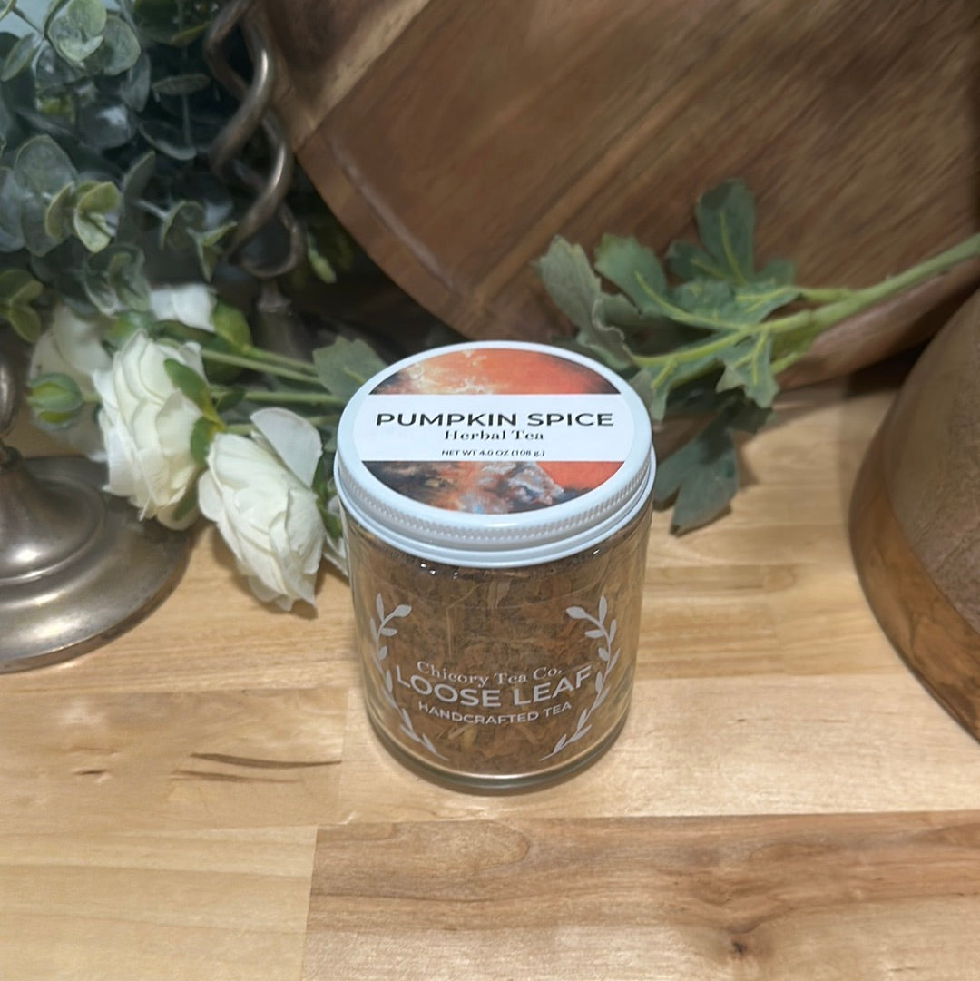 A more artistic photo of Chicory Tea Co.'s Pumpkin Spice Herbal Tea in the jar, view from front with flowers and a barrel in the background